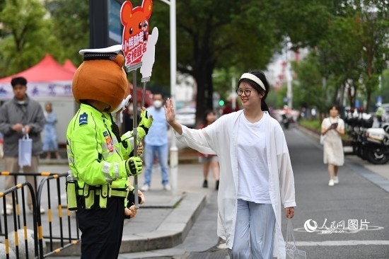 6月7日上午9時，隨著鈴聲的響起，2023年江西高考正式開考，江西省的53.57萬考生以縣（區(qū)）為單位隨機安排在全省256個考點、18968個考場參加高考。圖為“小熊交警”和考生擊掌鼓勵。 人民網(wǎng)記者 時雨攝