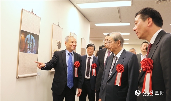 “湖州印象”攝影展主創(chuàng)、世界華人攝影協(xié)會副會長馮學(xué)敏向吳江浩大使、福田康夫前首相等嘉賓介紹展出作品。（人民網(wǎng) 許可攝）