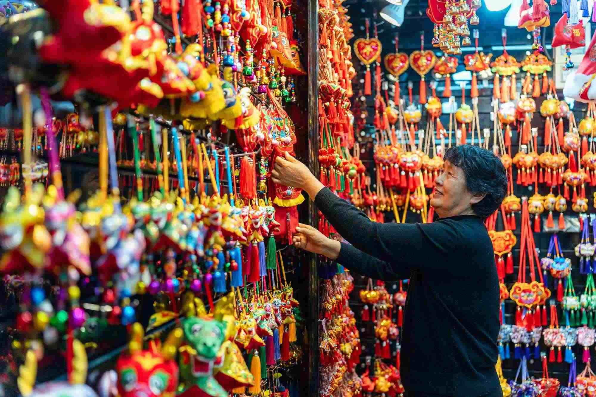 2023年12月11日，金華義烏國(guó)際商貿(mào)城，龍年喜慶用品掛滿攤位，顧客正在挑選中。