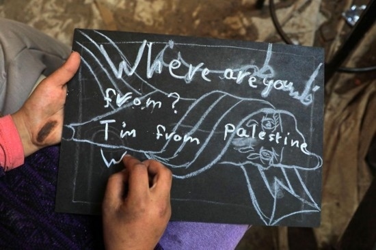 2023年12月28日，一名學生在加沙地帶南部城市拉法一所學校的臨時教室中寫下“我來自巴勒斯坦”的字樣。新華社發(fā)（里澤克·阿卜杜勒賈瓦德攝）