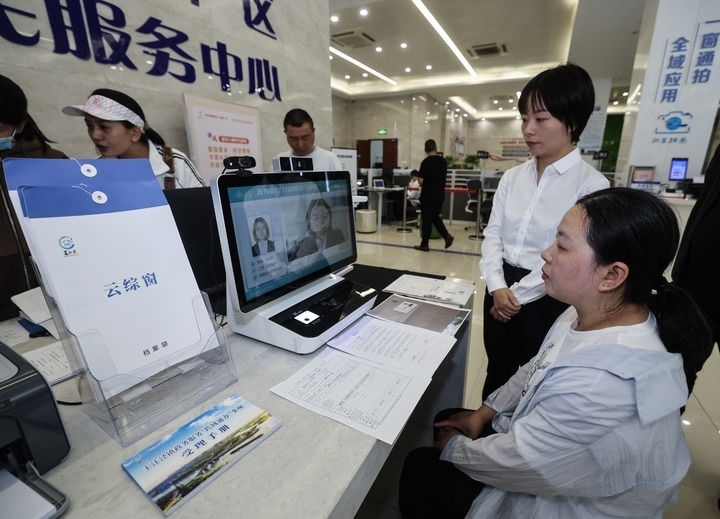 在浙江省嘉興市秀洲區(qū)王江涇鎮(zhèn)便民服務(wù)中心的“跨域通辦·云綜窗”窗口，辦理開(kāi)業(yè)登記的個(gè)體工商戶（右一）通過(guò)該系統(tǒng)與江蘇省蘇州市吳江區(qū)盛澤鎮(zhèn)行政審批局工作人員視頻連線，進(jìn)行身份讀取及材料線上審核（2024年5月9日攝）。新華社記者 徐昱 攝