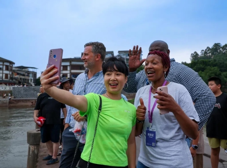 2024“一帶一路”媒體合作論壇聯(lián)合采訪調(diào)研行成員在樂(lè)山蘇稽古鎮(zhèn)與游客合影留念。本報(bào)記者 伊霄攝