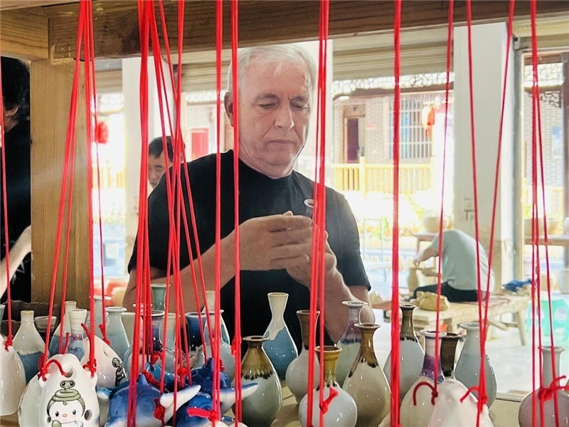 鄉(xiāng)愁如同一根根紅線，將游子與故鄉(xiāng)永遠(yuǎn)地牽連到一起?；逄账囄幕瘎?chuàng)意一條街的母氏陶藝館內(nèi)，紅線吊著陶瓶，思緒游走萬里。摩爾多瓦“信息標(biāo)簽”通訊社社長亞歷山大·塔納斯端詳著館內(nèi)展示的陶藝作品，并挑選出心儀的小擺件帶回摩爾多瓦，也帶走花茂村的“鄉(xiāng)愁”。（張亞欣攝）
