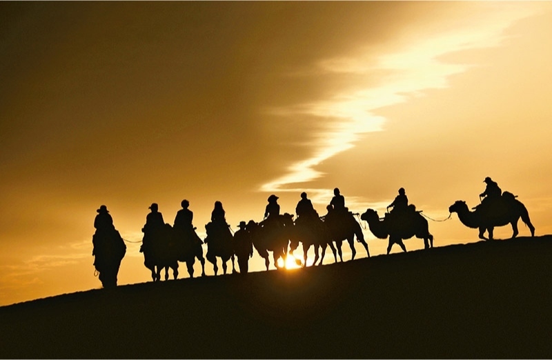 新時(shí)代以來(lái)，文化和旅游深度融合發(fā)展體制機(jī)制不斷健全，成功走出了一條獨(dú)具特色的中國(guó)旅游發(fā)展之路。圖為2024年9月1日清晨，游客在甘肅省敦煌市鳴沙山月牙泉景區(qū)乘騎駱駝，欣賞大漠風(fēng)光，體驗(yàn)絲路風(fēng)情。 新華社發(fā) 張曉亮/攝