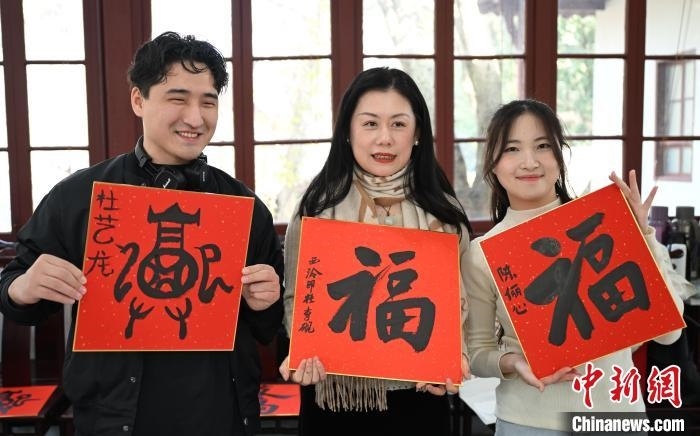 1月20日，外籍留學(xué)生和西泠印社社員李硯(中)展示各自創(chuàng)作的福貼。當日，來自巴西、馬來西亞、加納、哈薩克斯坦的外籍留學(xué)生在浙江杭州西泠印社體驗福貼、春聯(lián)和篆刻，感受古老的中國傳統(tǒng)文化。中新社記者 王剛 攝